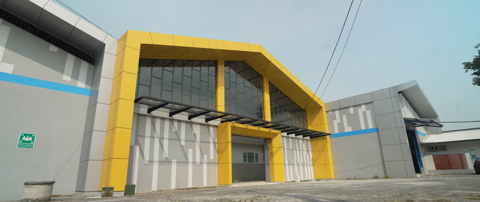 Fasad pintu masuk pabrik dengan bingkai kuning dan dinding abu-abu.