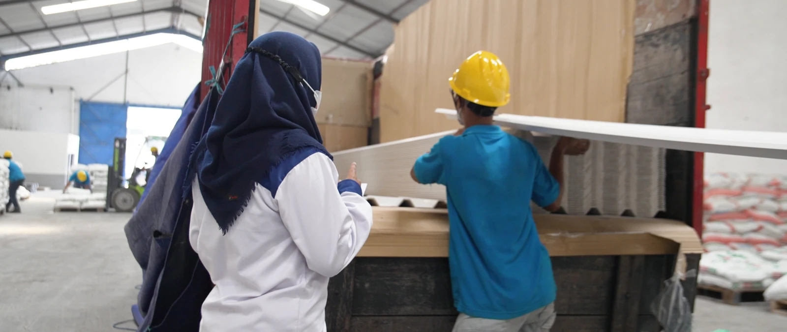 Staf dan pekerja memuat profil panjang ke kendaraan angkut di gudang.
